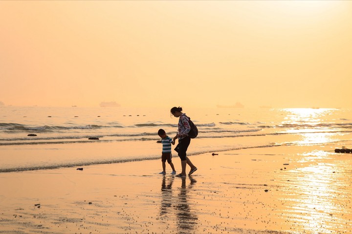A parent and child walking on the beach at sunset