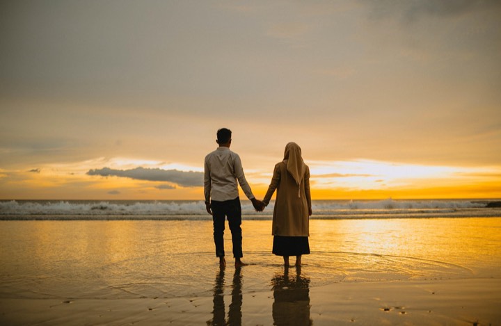 A couple holding hands on the beach at sunset
